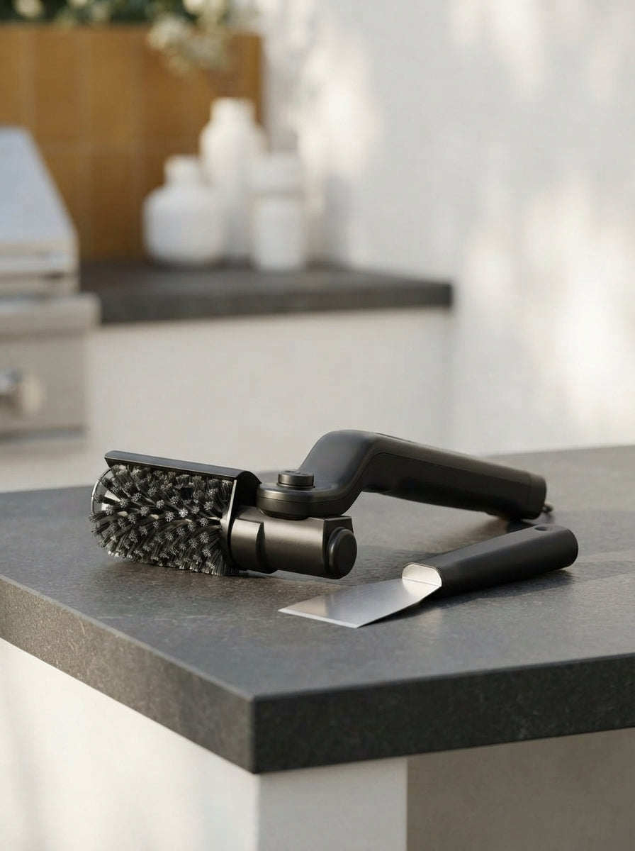 A professional-grade grill brush with a reinforced head and ergonomic handle on a dark stone counter in a modern outdoor kitc